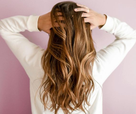 Obraz ukazuje kobietę z długimi włosami podanymi zabiegowi balejażu.